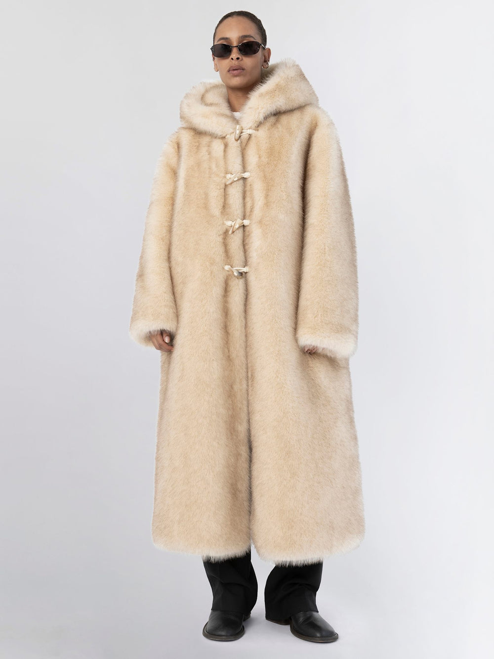 A model wearing a luxurious beige MEOTINE fur coat with a hood, styled with knee-high brown boots against a neutral backdrop.