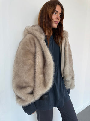 A model showcases a cozy, oversized beige fur jacket from MEOTINE, paired with a dark top and relaxed pants against a minimalist backdrop.