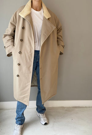A model wearing a beige oversized coat with a fluffy collar, paired with a white t-shirt and blue jeans, showcasing MEOTINE style.