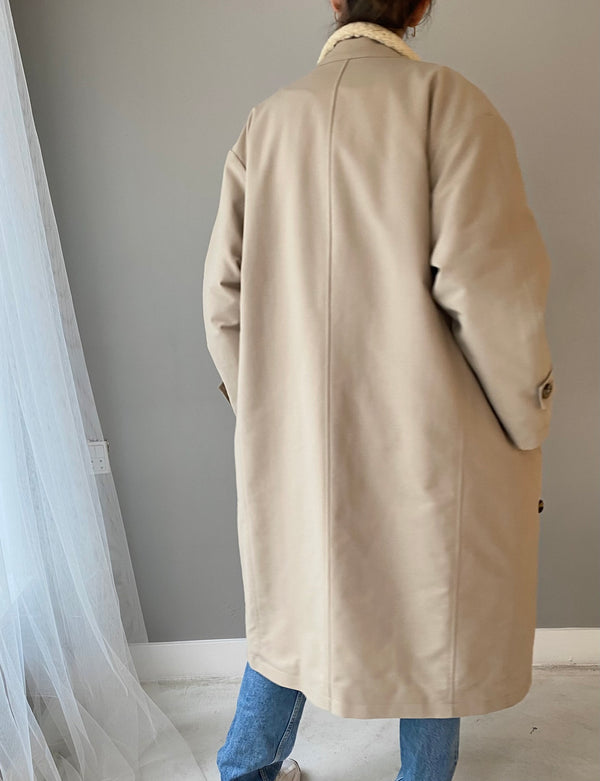 A woman wearing a beige MEOTINE coat stands with her back to the camera, showcasing its relaxed fit and stylish design.