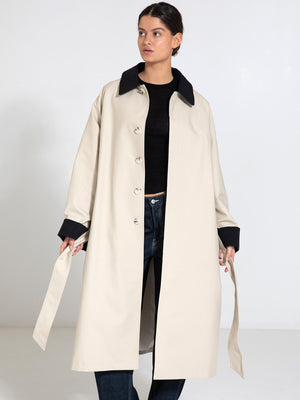 A model wears a stylish beige MEOTINE coat with a black collar, paired with a black top and jeans, showcasing a modern look.