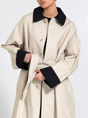 A model wears a stylish beige MEOTINE trench coat with a black collar and cuffs, showcasing a modern, oversized silhouette.