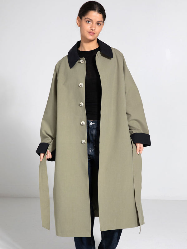A model showcases a stylish oversized olive green coat with a black collar and cuffs, featuring large buttons, by MEOTINE.