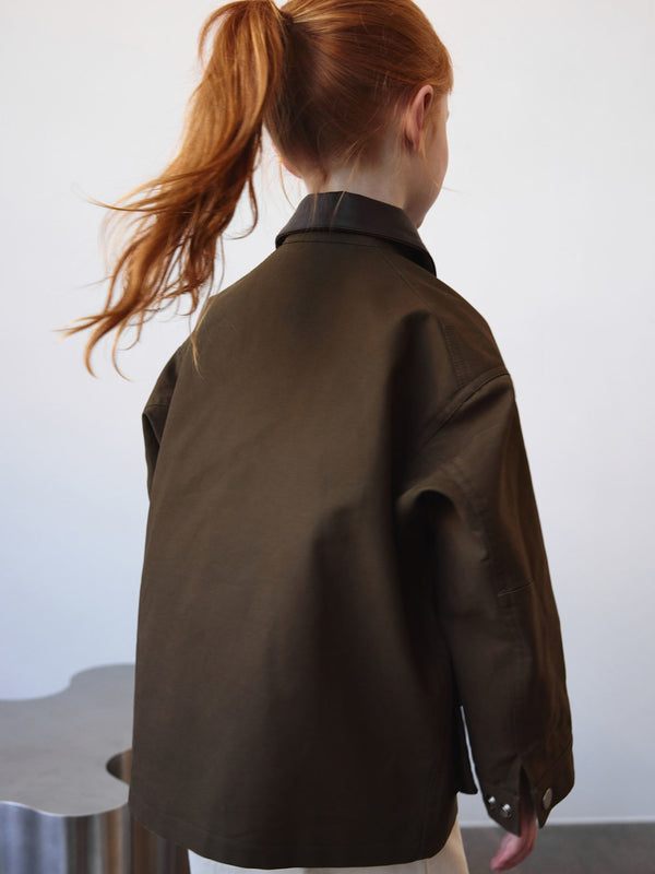 A girl with red hair wears a stylish brown MEOTINE jacket, showcasing a modern, relaxed fit from the back.