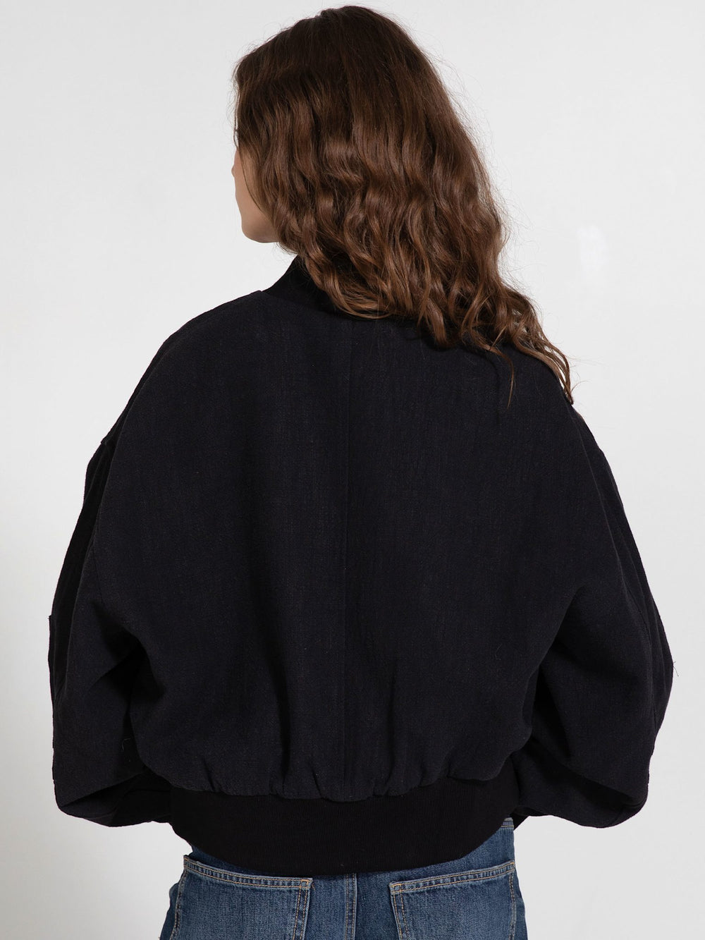 A model poses in a stylish black cropped jacket with oversized sleeves, paired with relaxed denim jeans, showcasing MEOTINE's trendy design.