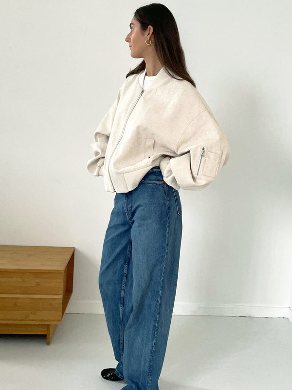 A model showcases a stylish oversized cream bomber jacket paired with loose blue jeans, embodying a relaxed, modern look. MEOTINE.