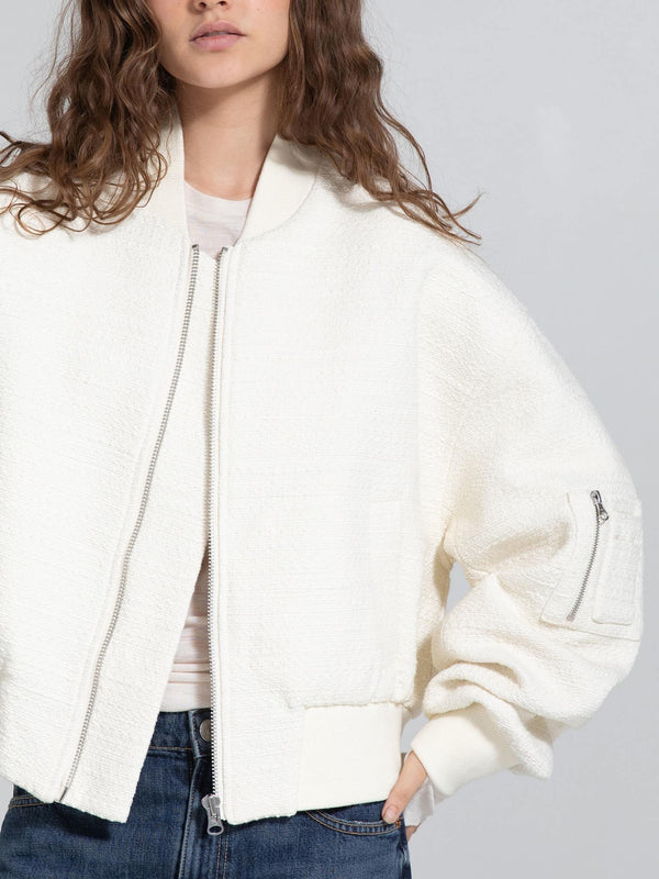 White textured bomber jacket with a zip closure and oversized sleeves, styled with a casual top and denim jeans. MEOTINE brand.