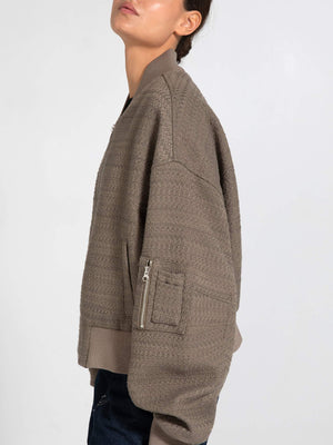 A model showcases a stylish, oversized taupe bomber jacket with a textured finish and zippered pocket, by MEOTINE.