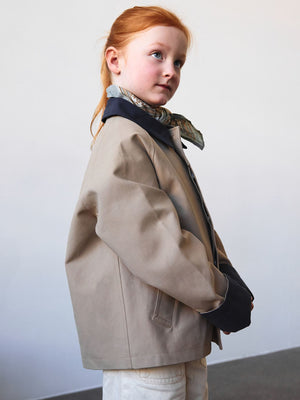 A young girl poses in a stylish beige jacket with a navy collar, showcasing MEOTINE's modern and chic design.