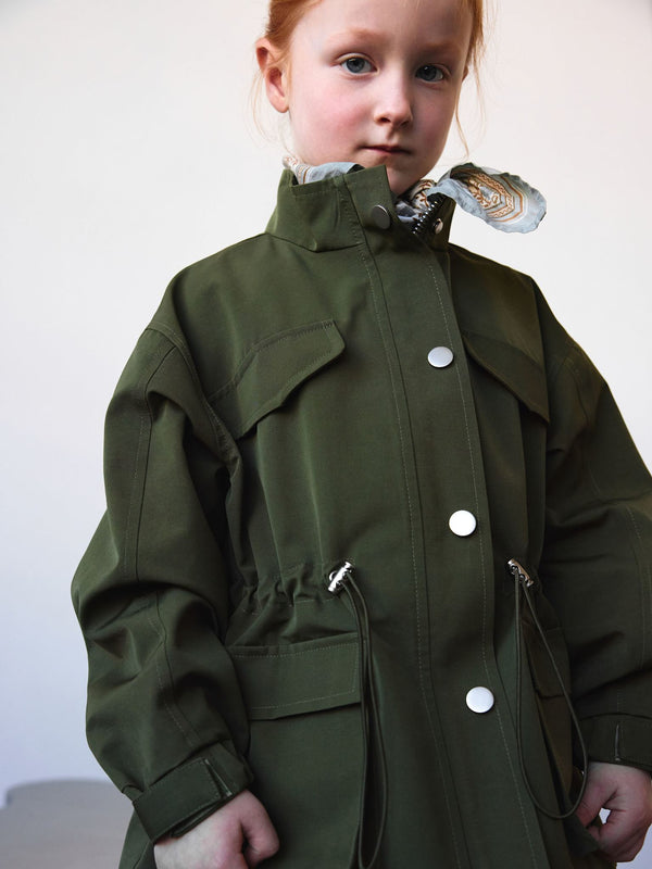 A young girl models a stylish green MEOTINE jacket with a cinched waist and snap buttons, showcasing a modern, trendy design.