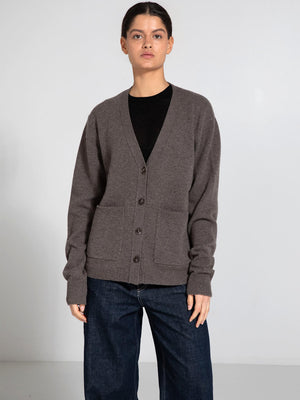 A model wears a cozy, brown cardigan with a V-neck and button closure, featuring two front pockets, by MEOTINE.