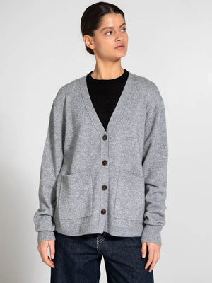A woman models a cozy gray cardigan with a V-neck and button closure, featuring two front pockets, by MEOTINE.
