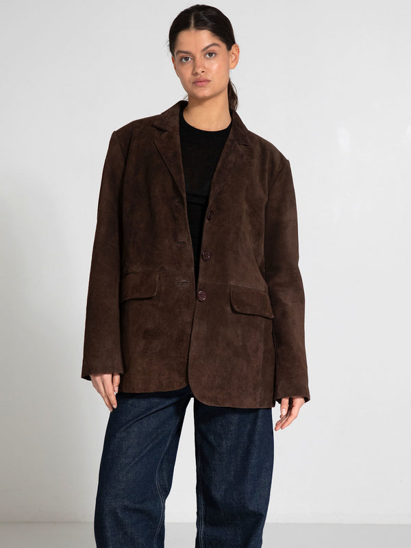 A model wears a brown suede blazer with a relaxed fit, paired with dark denim pants, showcasing MEOTINE's stylish design.