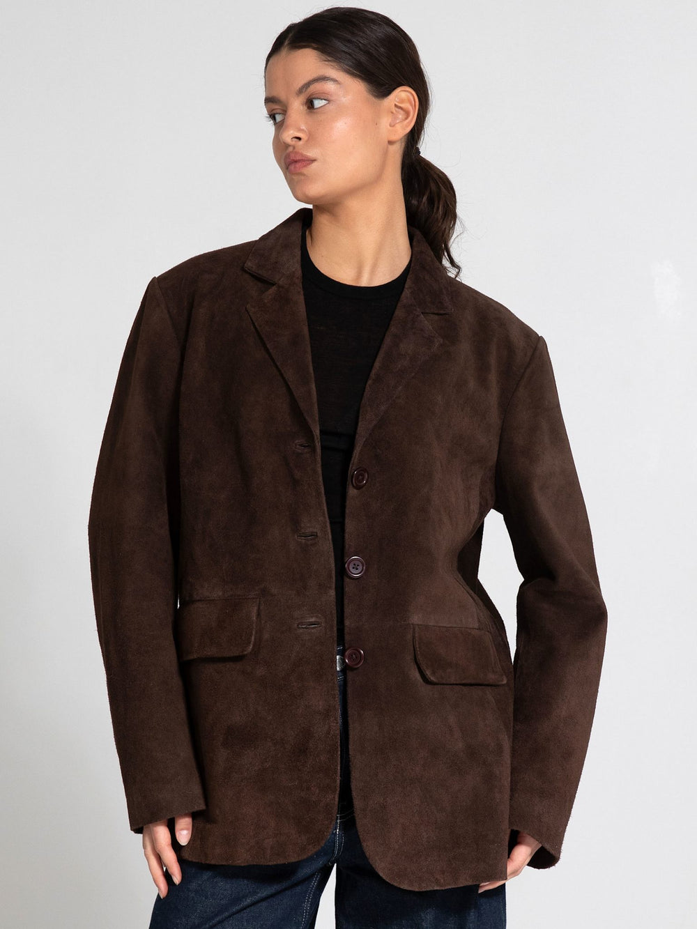 A model showcases a brown suede blazer with a relaxed fit, featuring a button closure and two front pockets, by MEOTINE.