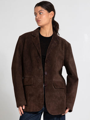 A model showcases a brown suede blazer with a relaxed fit, featuring a button closure and two front pockets, by MEOTINE.