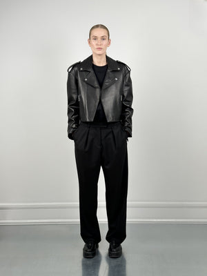 A model showcases a stylish black leather jacket paired with loose black trousers, embodying a chic, modern look by MEOTINE.