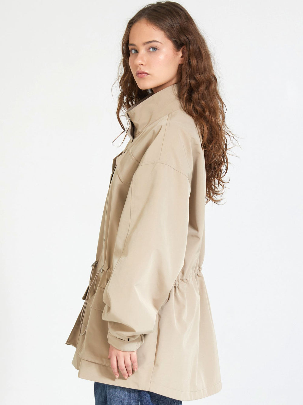A model wearing a beige MEOTINE jacket with a cinched waist and large pockets, styled with loose blue jeans.