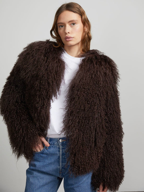 A model wears a fluffy, dark brown MEOTINE jacket over a white shirt, paired with blue jeans, showcasing a stylish look.