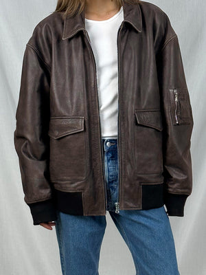 Brown leather jacket with a relaxed fit, featuring multiple pockets and a zip closure, styled with a white top and blue jeans. MEOTINE.