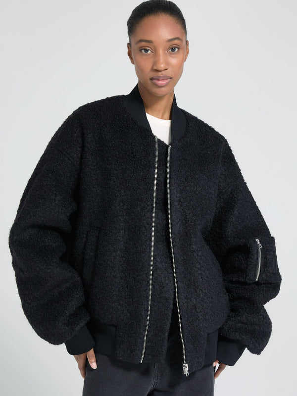 A model showcases a cozy black bomber jacket with a plush texture, featuring a zip closure and oversized sleeves by MEOTINE.
