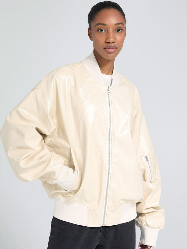 A model showcases a stylish cream-colored bomber jacket with a shiny finish, featuring a zip closure and ribbed cuffs. MEOTINE.