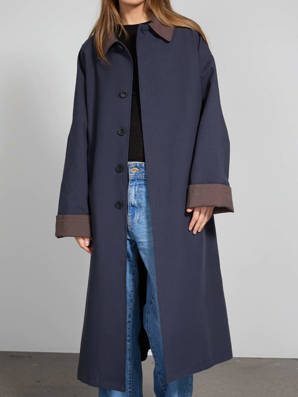 A model wears a long navy coat with contrasting brown cuffs, showcasing a stylish and modern look by MEOTINE.