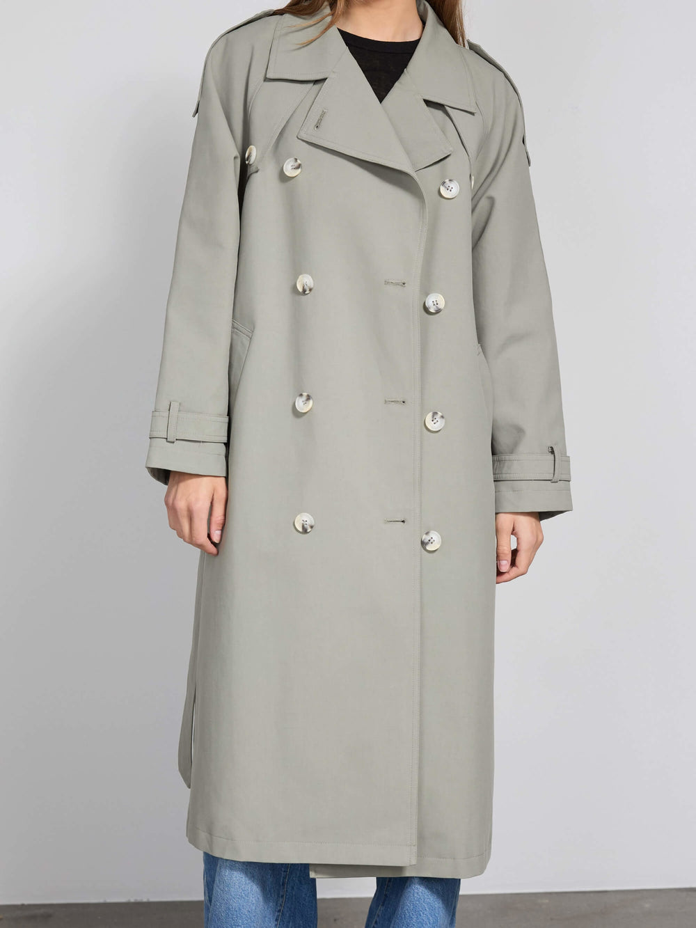 A model wears a stylish light gray trench coat with large buttons, paired with wide-leg jeans, showcasing MEOTINE's modern design.