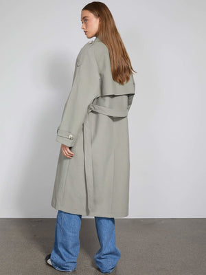 A model showcases a stylish light gray trench coat from MEOTINE, paired with blue jeans, standing against a neutral backdrop.