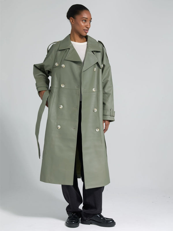 A model showcases a stylish green trench coat by MEOTINE, featuring a double-breasted design and a relaxed fit, paired with black pants.