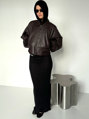 A model wearing a brown oversized bomber jacket and a black maxi skirt, exuding a chic, modern vibe with sunglasses. MEOTINE.