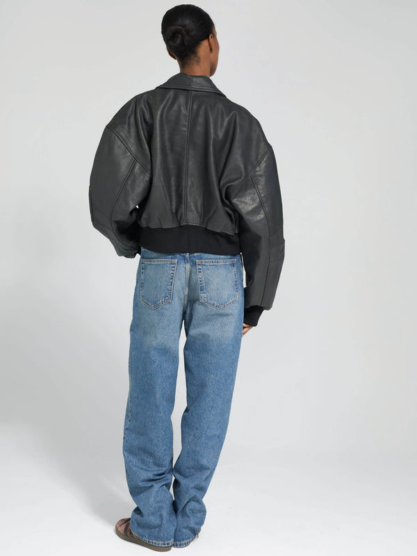 A model showcases a stylish black leather bomber jacket paired with relaxed blue jeans, embodying a modern, casual look by MEOTINE.
