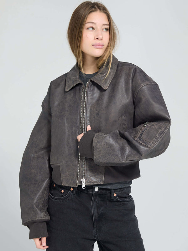 A model wears a stylish cropped black leather jacket from MEOTINE, paired with high-waisted black jeans, exuding a chic vibe.