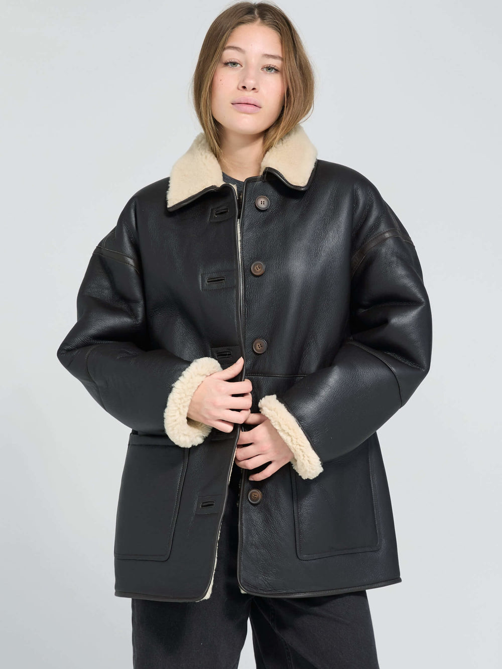 A model wears a stylish black MEOTINE jacket with a cozy beige fur collar, showcasing a chic and modern look.