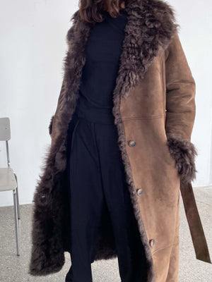 A model wears a luxurious brown MEOTINE coat with a plush fur collar, paired with a black outfit, showcasing elegance and warmth.