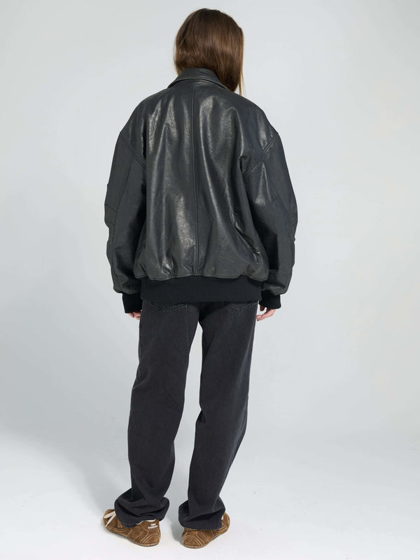 A model wearing a black oversized leather bomber jacket from MEOTINE, paired with dark pants, viewed from the back.