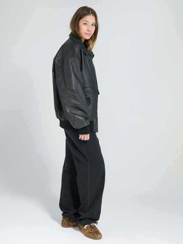 A model showcases a stylish black leather jacket paired with loose black pants, embodying a chic, modern look by MEOTINE.