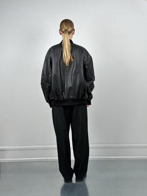 A model wearing a black oversized leather bomber jacket from MEOTINE, paired with loose black trousers, seen from the back.