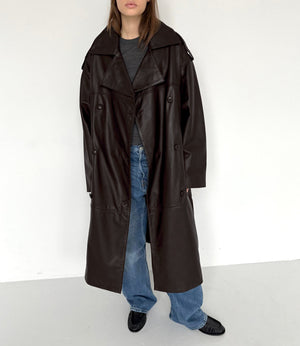 A model showcases a stylish brown leather trench coat paired with casual blue jeans, embodying modern fashion by MEOTINE.