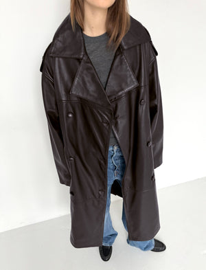 A model showcases a stylish brown leather trench coat by MEOTINE, paired with casual jeans and a gray top.