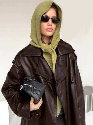 A model wearing a brown oversized leather coat and a green hooded sweater, holding a small black bag, showcasing MEOTINE style.