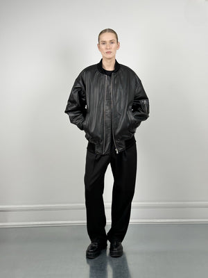 A model stands confidently in a black leather bomber jacket paired with loose black trousers, showcasing MEOTINE's stylish design.