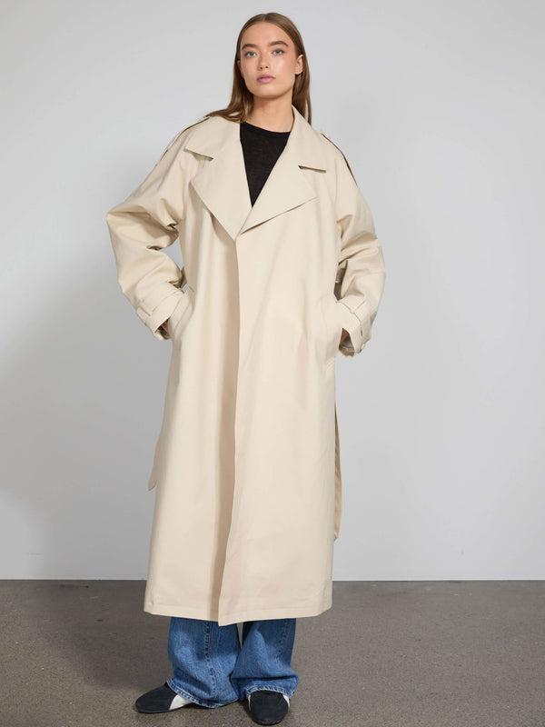 A model showcases a stylish beige trench coat with oversized pockets, paired with casual blue jeans, representing MEOTINE's chic aesthetic.