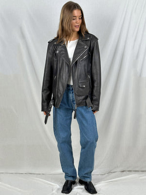 A model wearing a black leather biker jacket over a white top, paired with blue jeans and black ankle boots, showcasing MEOTINE style.