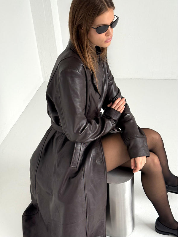 A model wearing a stylish brown leather coat from MEOTINE, seated on a metallic stool, exuding a chic and modern vibe.