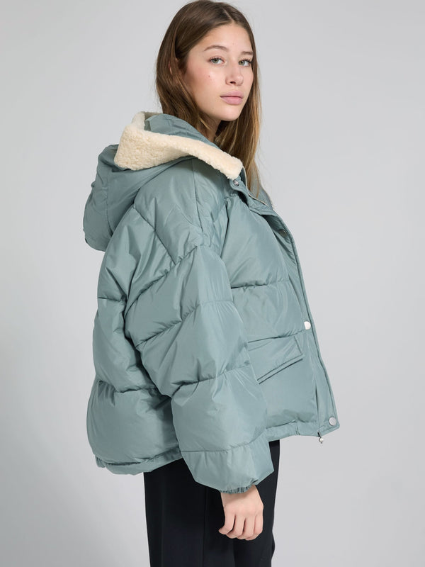 A model showcases a cozy, oversized teal puffer jacket with a soft cream hood, perfect for winter, by MEOTINE.