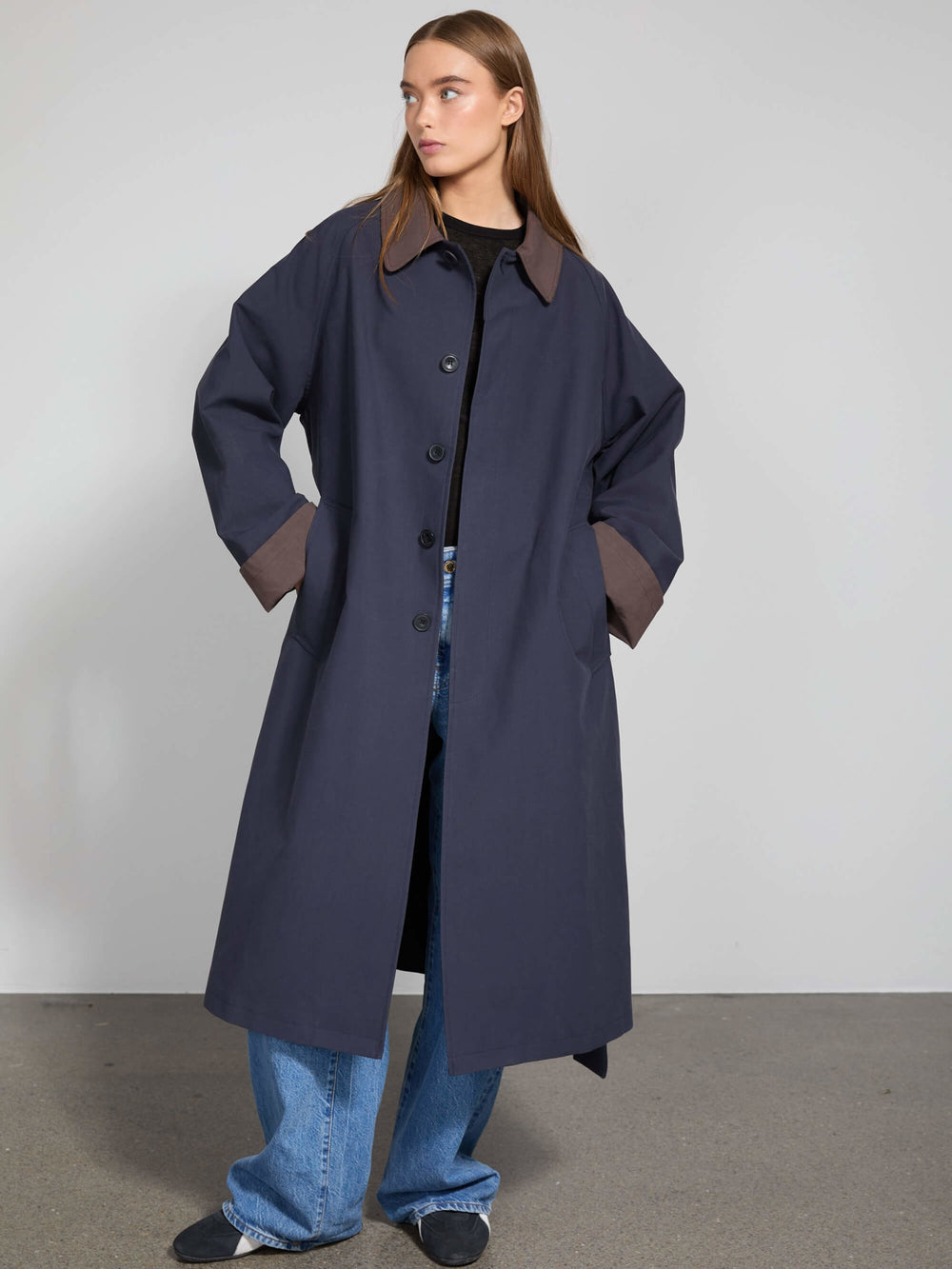 A model wears a long navy coat with contrasting brown cuffs, showcasing a stylish and modern look by MEOTINE.