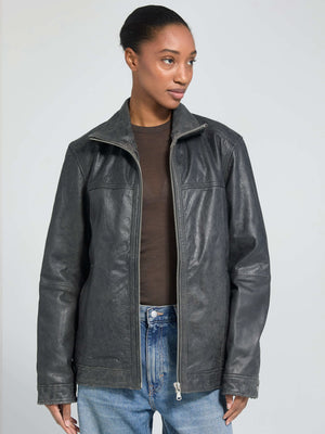 A woman models a stylish black leather jacket from MEOTINE, featuring a zip closure and a relaxed fit, paired with light jeans.
