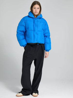 A model wears a vibrant blue cropped puffer jacket from MEOTINE, paired with loose black trousers, showcasing a stylish winter look.