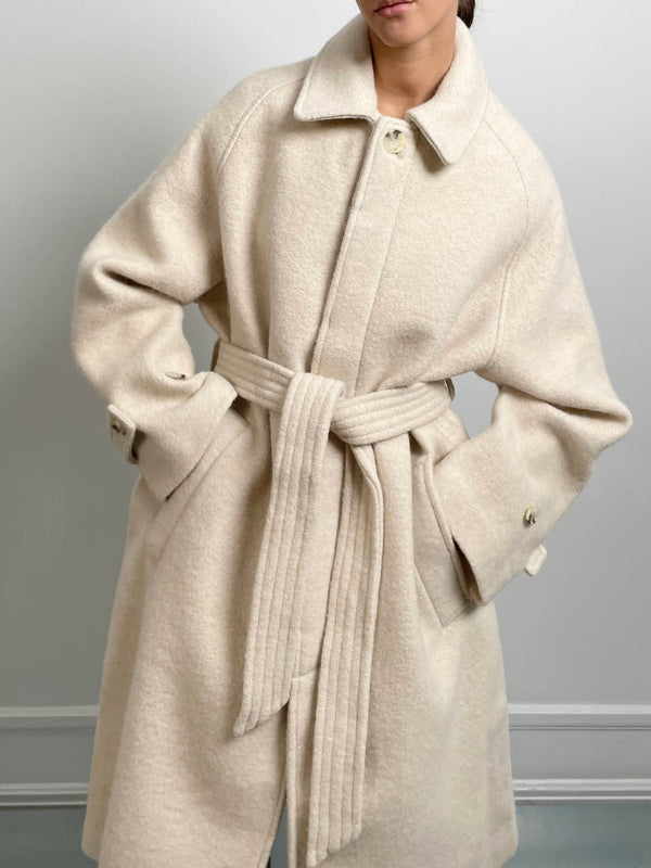 A model wears a cozy beige MEOTINE coat with a belted waist, featuring a classic collar and oversized fit, perfect for chilly days.