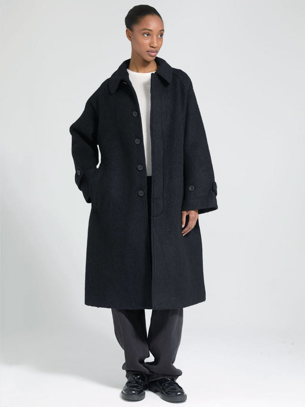 A model showcases a stylish black oversized coat with a button-up front, paired with relaxed trousers, embodying MEOTINE's chic aesthetic.